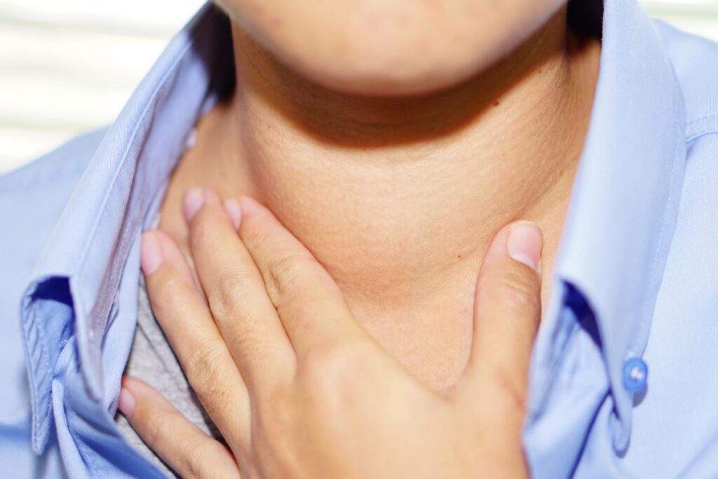 Close-up of a person touching their throat with fingers, wearing a blue shirt.