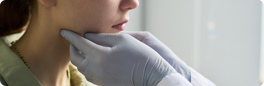 Close-up of gloved hands examining a woman's jawline during a medical checkup.