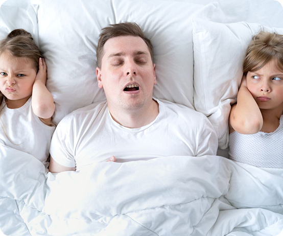Man sleeping in bed with his eyes closed, flanked by two children who cover their ears and look annoyed on either side of him.